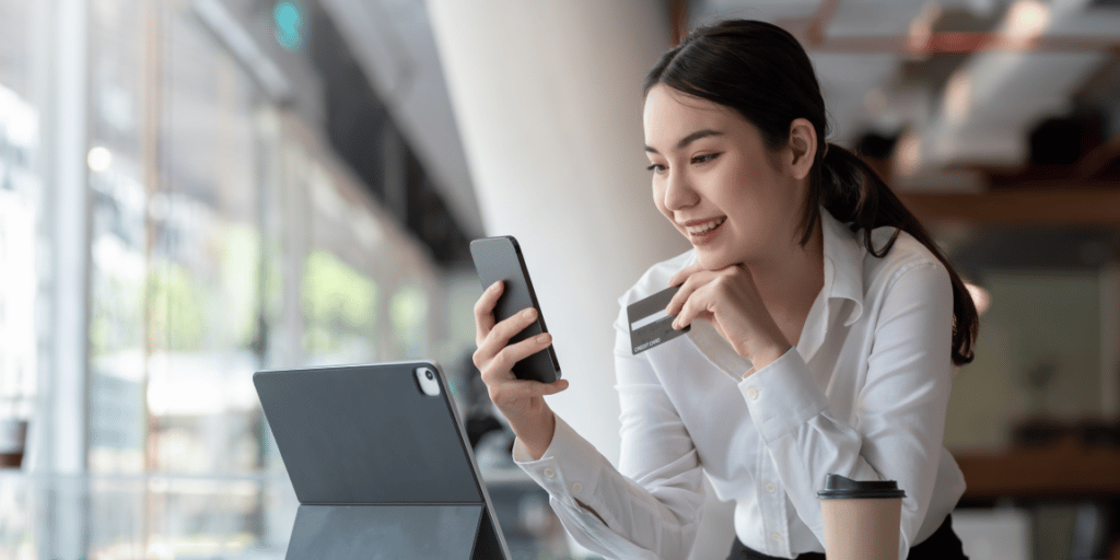 Empreendedora utilizando o seu cartão de crédito par autônomo, pelo celular, e ao fundo aparece o seu escritório.