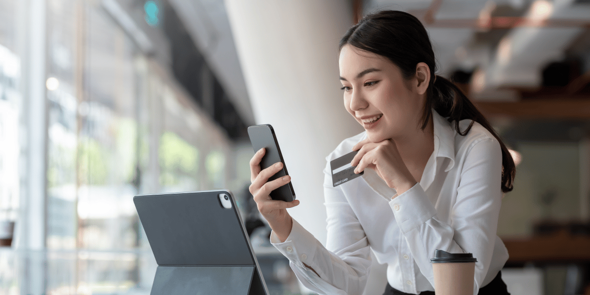 Empreendedora utilizando o seu cartão de crédito par autônomo, pelo celular, e ao fundo aparece o seu escritório.
