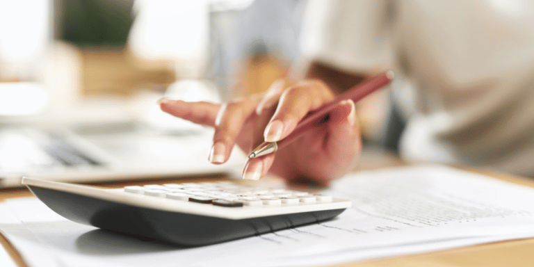 Pessoa empreendedora realizando o fechamento contábil empresarial em seu escritório, com documentos e uma calculadora na mesa.