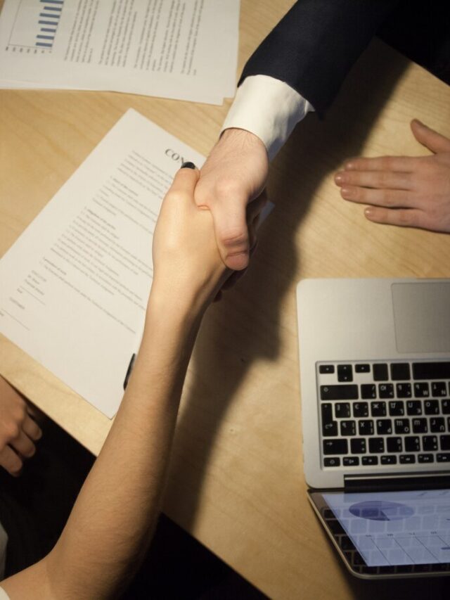 Duas pessoas apertando as mãos em um escritório, com documentos legais sobre a mesa, simbolizando um acordo amigável.