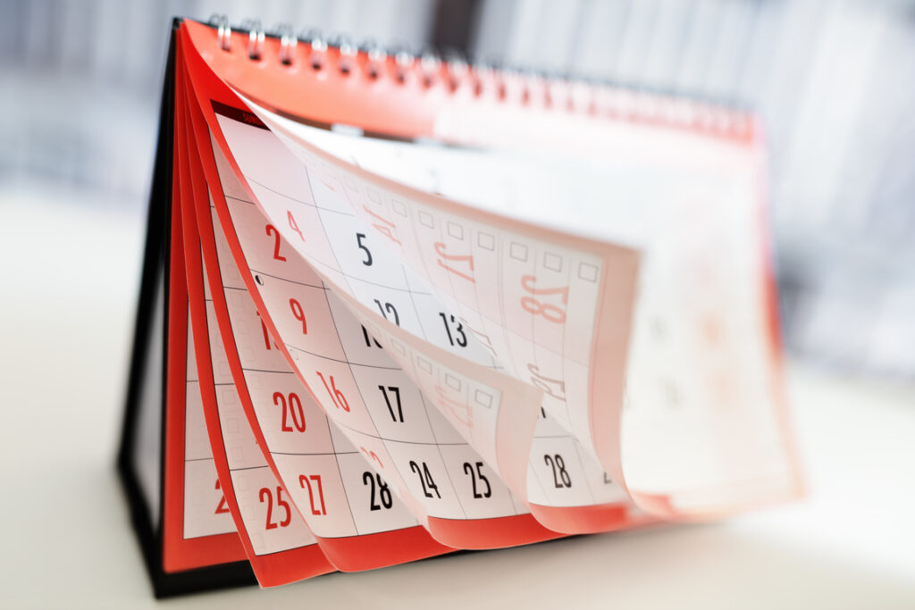 A imagem mostra um calendário de mesa de bordas vermelhas sendo folheado.