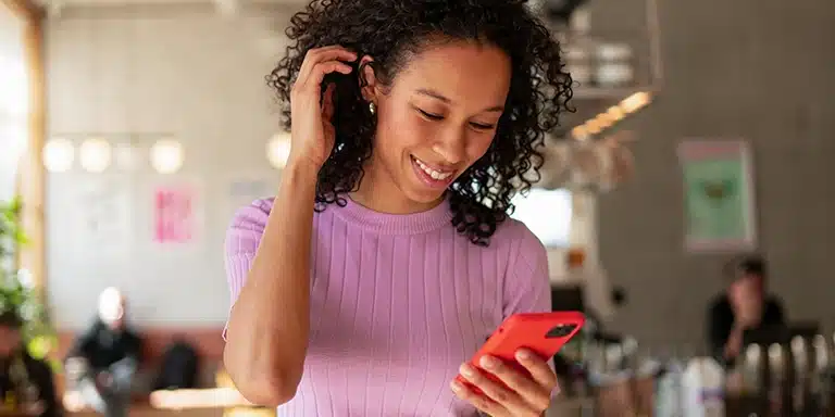 Mulher sorri ao olhar para a tela do celular, em imagem que ilustra artigo sobre comprovante do CNPJ