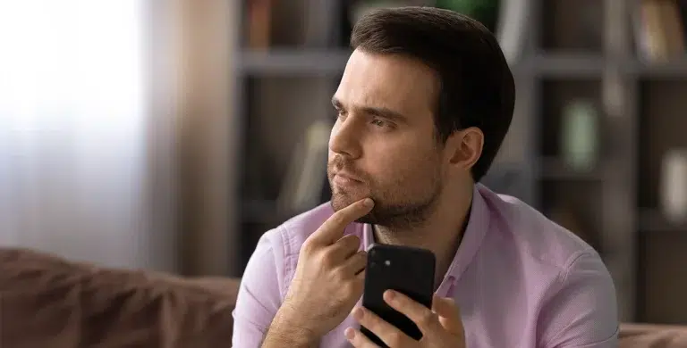 Homem está pensativo, enquanto segura celular em uma mão e toca o queixo com a outra, em imagem que ilustra artigo sobre profisisonais liberais terem conta PJ.