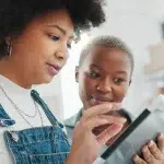 Mulher mexe em um tablet enquanto outra observa, em imagem que ilustra este artigo sobre diferenças entre bancos digitais e bancos tradicionais