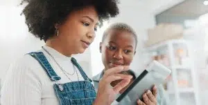 Mulher mexe em um tablet enquanto outra observa, em imagem que ilustra este artigo sobre diferenças entre bancos digitais e bancos tradicionais