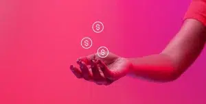 Fotomontagem de uma mão com a palma aberta para cima, com ícones de dinheiro sobre ela, ilustra este artigo sobre como cobrar clientes com régua de cobrança.