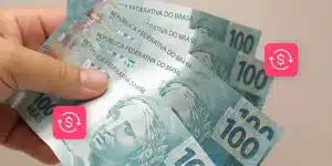Fotomontagem de uma mão segurando 5 notas de 100 reais, com ícones de empréstimo ao redor, para ilustrar artigo sobre capital de giro próprio ou de terceiros para empresas.