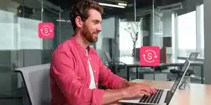 Fotomontagem de homem sorrindo ao utilizar um laptop ilustra artigo sobre diferenças entre crédito rotativo PJ e capital de giro