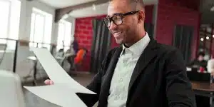 Homem sorri ao ler documentos, em imagem que ilustra artigo sobre as diferenças entre desconto de duplicatas e antecipação de boletos