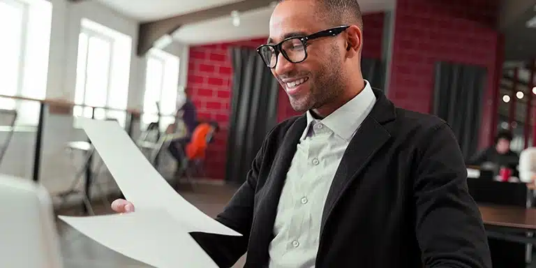 Homem sorri ao ler documentos, em imagem que ilustra artigo sobre as diferenças entre desconto de duplicatas e antecipação de boletos