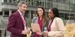 Um homem e duas mulheres sorriem enquanto observam o tablet segurado por uma delas, em imagem que ilustra artigo sobre o que considerar antes de escolher a melhor conta PJ para sua empresa.