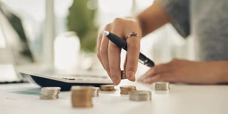 Pessoa segurando uma caneta enquanto empilha moedas sobre uma mesa, em imagem que ilustra artigo sobre capital de giro.