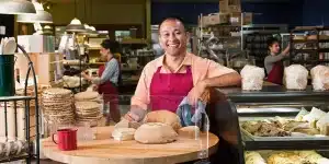 Homem que trabalha em uma padaria sorri, em imagem que ilustra artigo sobre MEI, Simples, Lucro Presumido e Lucro Real.