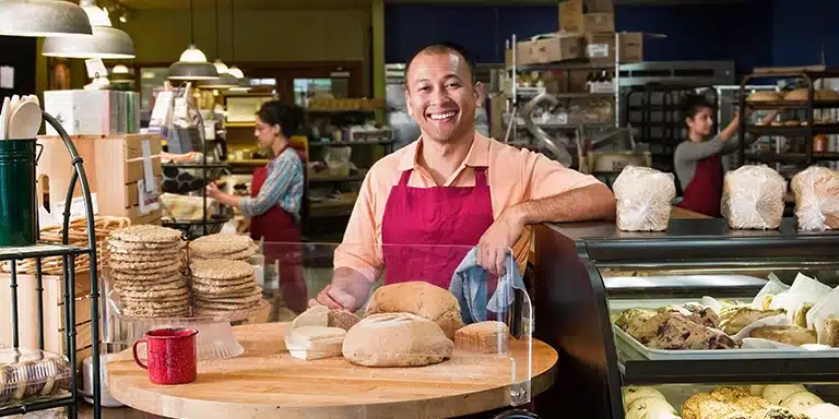 Homem que trabalha em uma padaria sorri, em imagem que ilustra artigo sobre MEI, Simples, Lucro Presumido e Lucro Real.