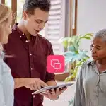 Homem mostra informações de um tablet para duas mulheres. Ao redor, há ícones de comunicação digital, em fotomontagem que ilustra artigo sobre marketing multicanal.