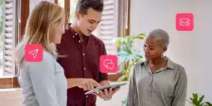 Homem mostra informações de um tablet para duas mulheres. Ao redor, há ícones de comunicação digital, em fotomontagem que ilustra artigo sobre marketing multicanal.