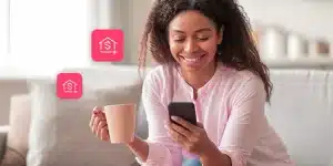 Mulher sorri olhando para a tela do celular, enquanto segura uma caneca de café na outra mão, em imagem que ilustra como receber rendimentos de aluguel em uma conta PJ.