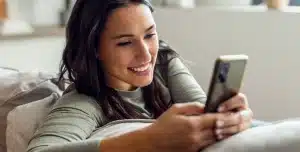 Mulher sorri ao digitar em seu smartphone, em imagem que ilustra artigo sobre com abrir uma conta PJ.