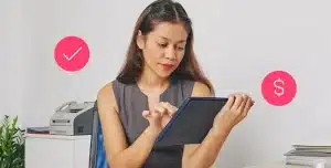 Mulher utiliza tablet em fotomontagem com ícones de check e dinheiro, que ilustra artigo sobre CND/CRF do FGTS para empresas.