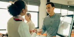 Homem entrega documento para mulher em escritório, em imagem que ilustra artigo sobre abono salarial para empresas