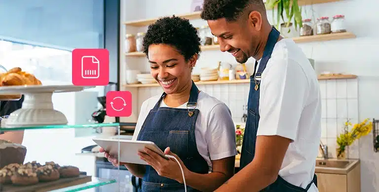 Duas pessoas sorrim enquanto observam um tablet em uma panificadora. Na fotomontagem, que ilustra artigo sobre boletos recorrentes e Pix Automático, há também ícones financeiros.