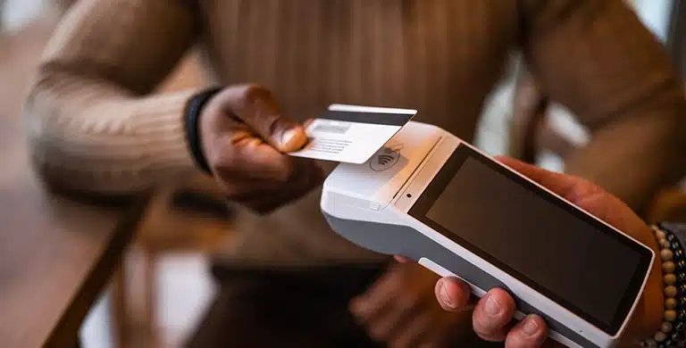 Pessoa efetua pagamento com um cartão em uma maquininha, em imagem que ilustra artigo sobre Cartão PJ para equipes externas: como funciona controle e reembolsos de colaboradores