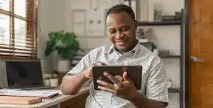 Homem sorri ao utilizar tablet, em imagem que ilustra artigo sobre como fazer e-CNPJ para empresa, o certificado digital de pessoa jurídica.