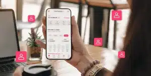 Fotomontagem da tela do app da conta PJ da Cora em um smartphone segurado por uma pessoa, com diversos ícones que representam diferentes usuários.