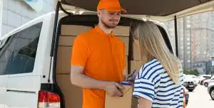 Homem de uniforme laranja faz entrega de caixa para uma mulher, que assina um documento, em imagem que ilustra artigo sobre como fazer uma política de pagamento de fornecedores.
