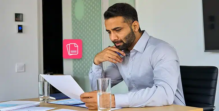 Homem sentado e com um braço apoiado na mesa do escritório analisa um documento, em fotomontagem com ícone de boleto que ilustra artigo sobre boleto pago em duplicidade pela empresa.