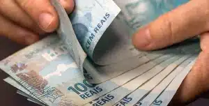 Mãos segurando notas de 100 reais, em imagem que ilustra artigo sobre risco-sacado para empresas.