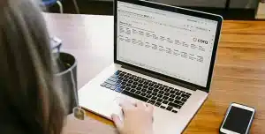 Mulher utiliza laptop, que na tela tem uma planilha de controle financeiro desenvolvida pela Cora.