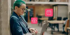 Mulher utiliza seu laptop em pé, encostada numa parede. Fotomontagem que ainda conta com ícones de agendamento e de finanças ilustra artigo sobre automação de boletos recorrentes para reduzir inadimplência.