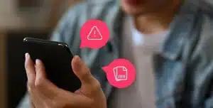Pessoa segurando um smartphone com a mão, com ícones gráficos de alerta e de cartão sobrepostos à imagem.