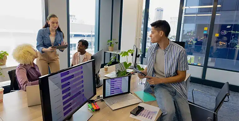 Pessoas em escritório, ao redor de mesas com computadores, notebook e tablet exibindo gráficos, em imagem que ilustra artigo sobre planejamento de crédito empresarial 2026.