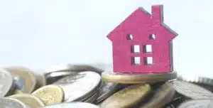 Casa em miniatura posicionada sobre moedas, em imagem que ilustra artigo sobre como imobiliárias podem reduzir inadimplência em aluguéis com gestão de cobranças moderna.