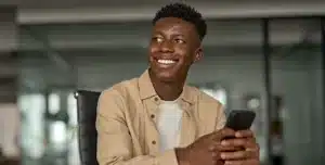 Pessoa sentada em ambiente interno, segurando um smartphone e sorrindo, em imagem que ilustra artigo sobre se conta PJ da Cora é boa para MEI em 2026.