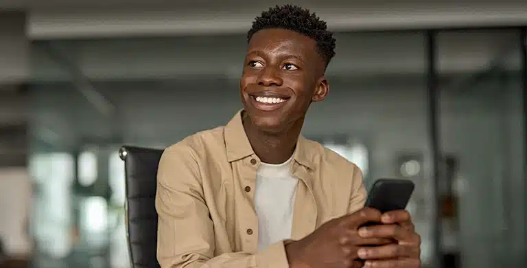 Pessoa sentada em ambiente interno, segurando um smartphone e sorrindo, em imagem que ilustra artigo sobre se conta PJ da Cora é boa para MEI em 2026.