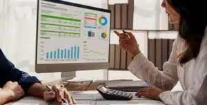 Pessoas analisando gráficos financeiros em um monitor durante reunião, em imagem que ilustra artigo sobre conta PJ integrada ao sistema de cobrança para prestadores de serviço.