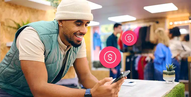 Pessoa usando smartphone em ambiente comercial, com ícones de dinheiro sobrepostos à imagem, em imagem que ilustra artigo sobre centralizar recebíveis em uma conta PJ.