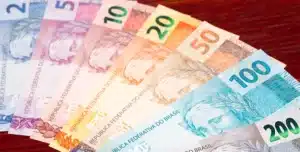 Imagem de cédulas de real organizadas em leque sobre superfície de madeira, ilustra artigo sobre comparação de bancos para empréstimo PJ.