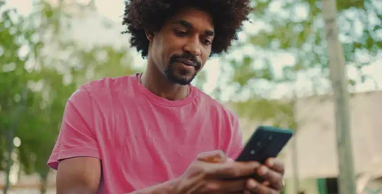 Pessoa em ambiente externo, segurando um smartphone e olhando para a tela, em imagem que ilustra artigo sobre entenda quando vale a pena trocar seu tradicional banco PJ por uma opção mais moderna.