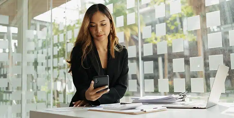 Pessoa em ambiente interno, segurando um smartphone sobre mesa com papéis e notebook, em imagem que ilustra artigo sobre quanto custa manter uma conta PJ em 2026.