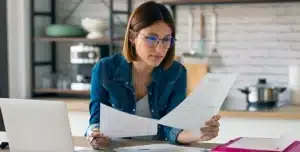 Pessoa sentada à mesa, analisando documentos impressos ao lado de notebook aberto, em imagem que ilustra artigo sobre trocar de banco PJ para reduzir custos.