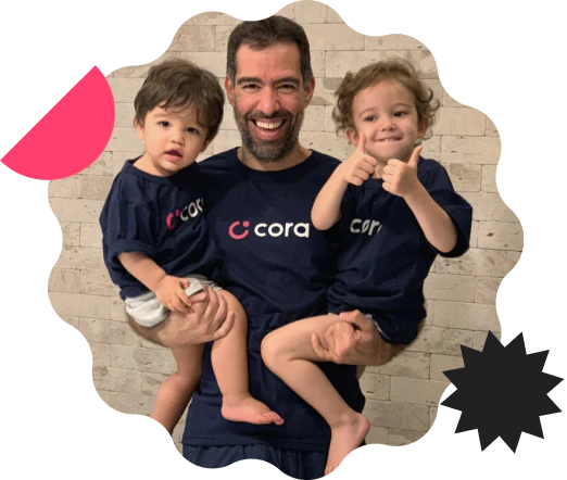 Pai com seus filhos nos braços, no braço direito um menino e no braço esquerda uma menina, todos com camiseta azul escrito Cora.